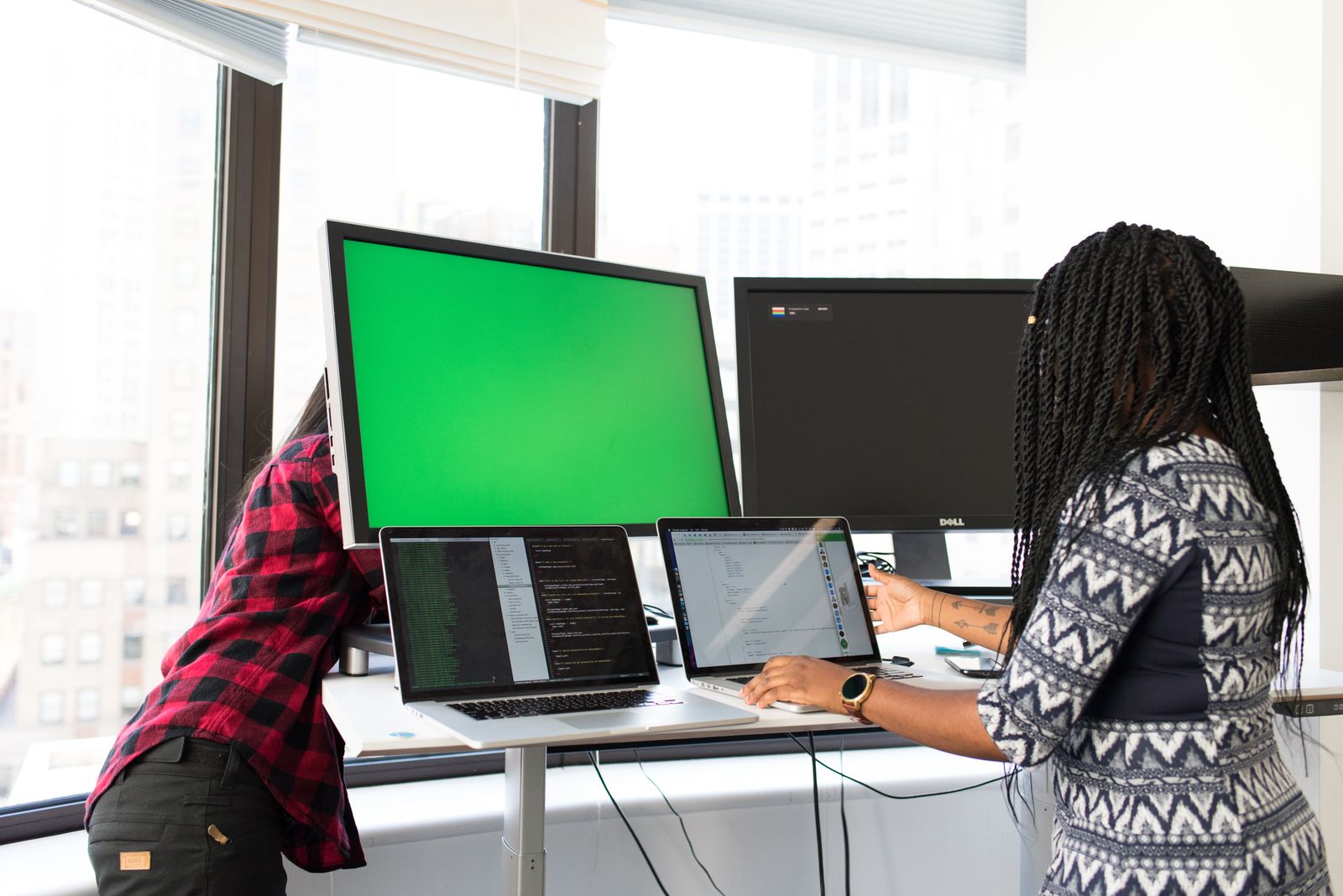 Two colleagues working across laptops and monitors in a bright modern office