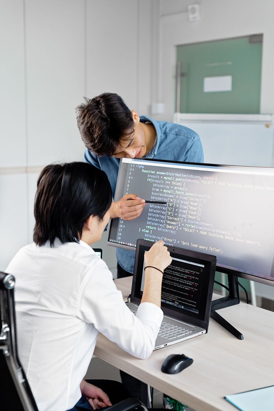 Two engineers reviewing application code together across monitors in a bright office