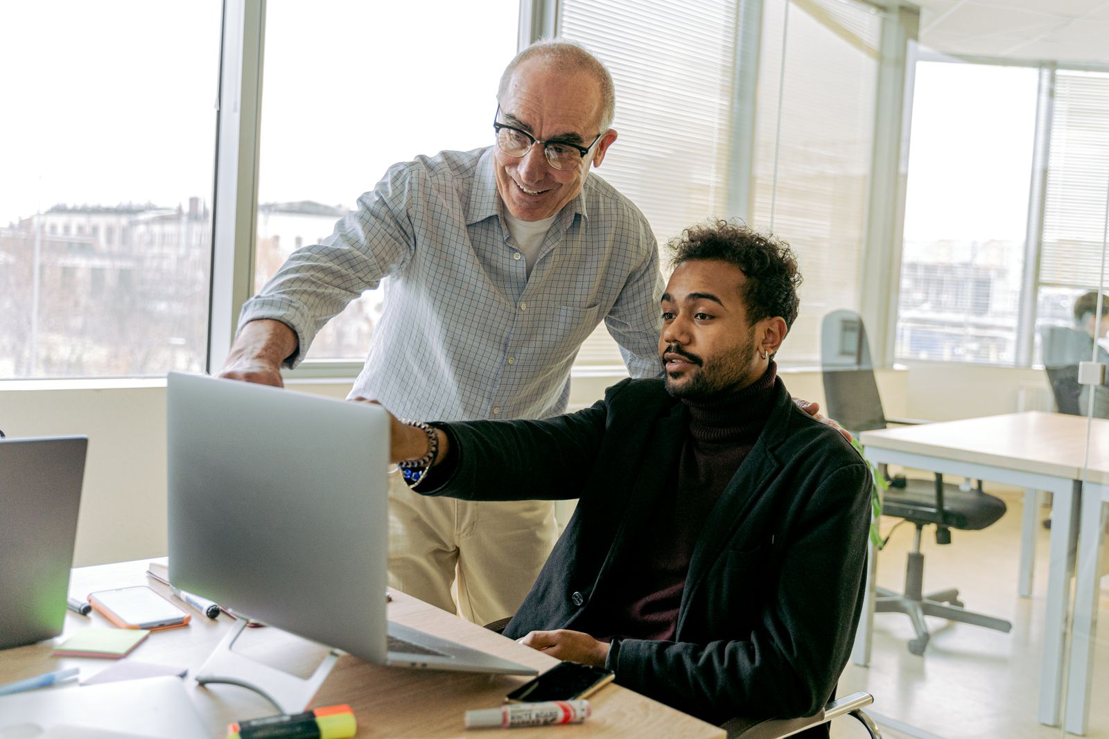 A colleague helping another with a laptop issue in a bright office