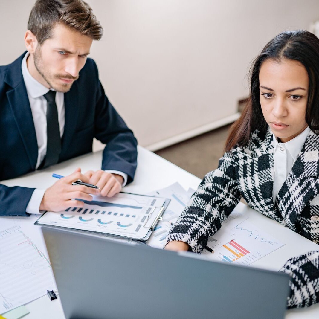 A man and a woman reviewing business analysis charts together at a bright office desk