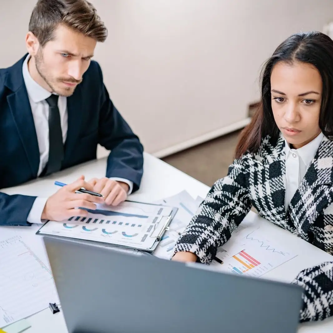 A man and a woman reviewing business analysis charts together at a bright office desk