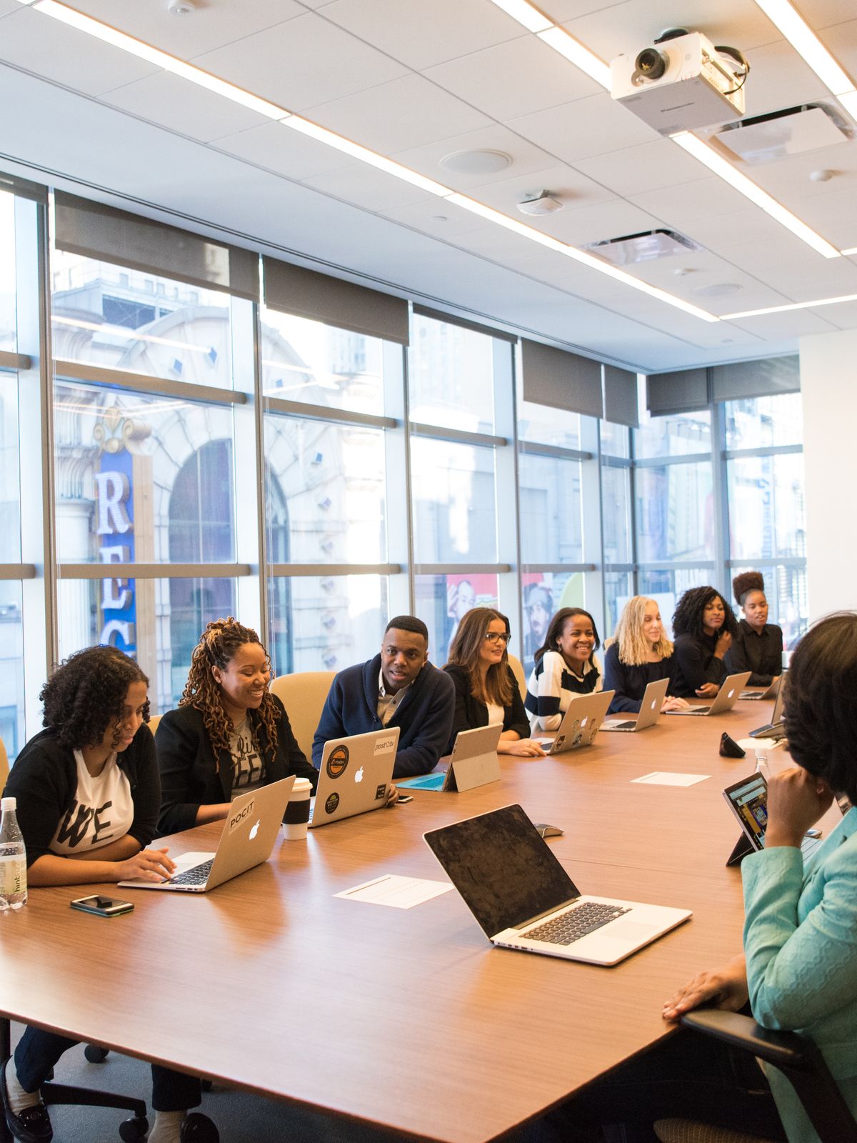 People seated around a long boardroom table with laptops beside floor-to-ceiling windows