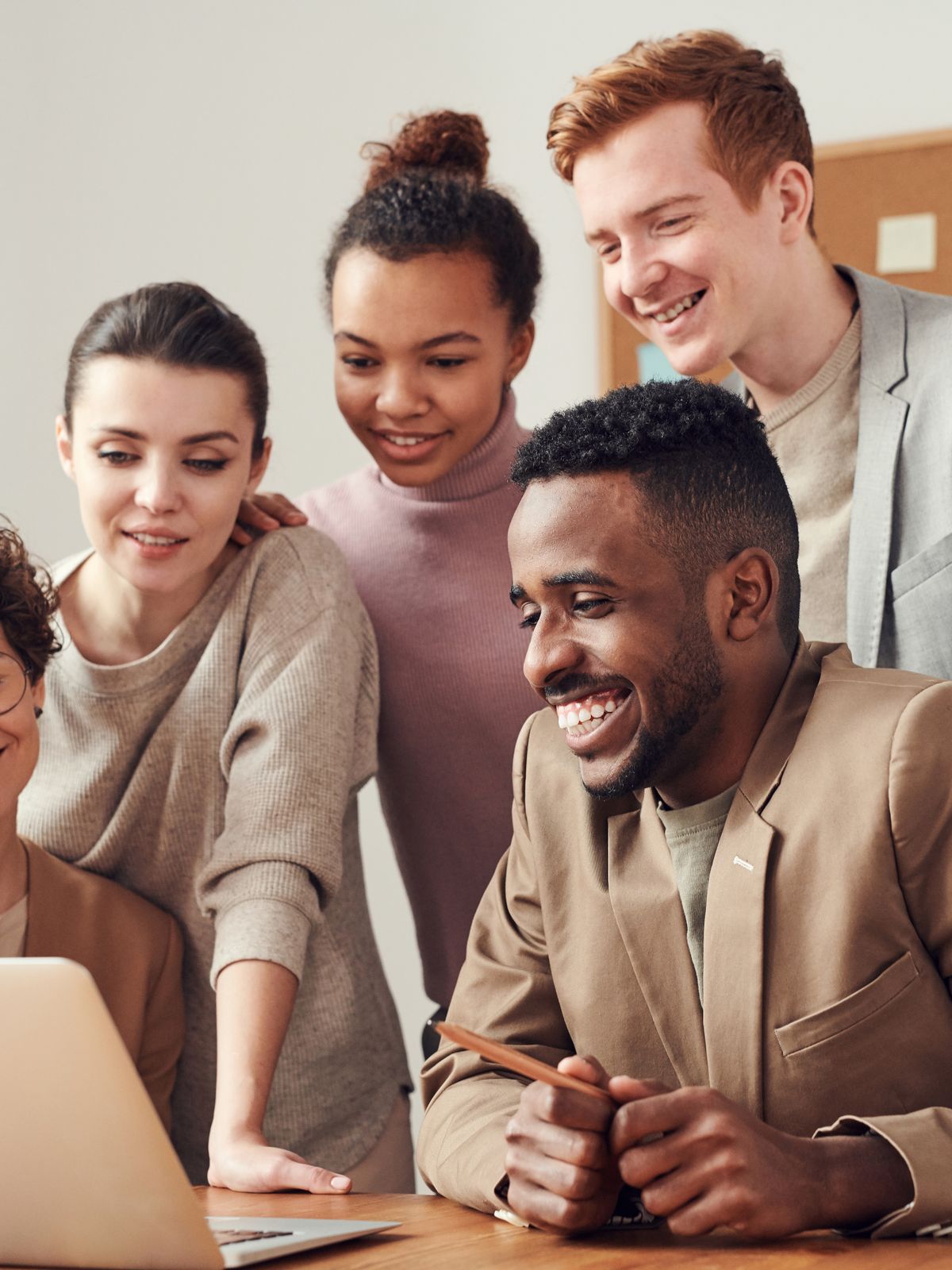 A diverse group of colleagues smiling around a laptop at a wooden table