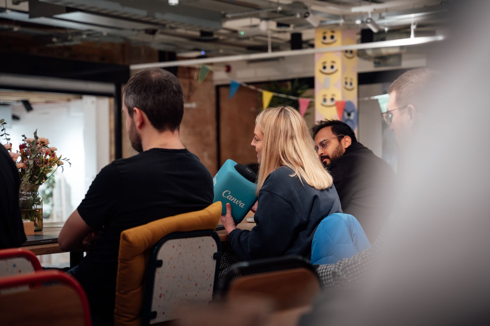 People seated at a table in a bright creative office during an event, one woman holding a teal box