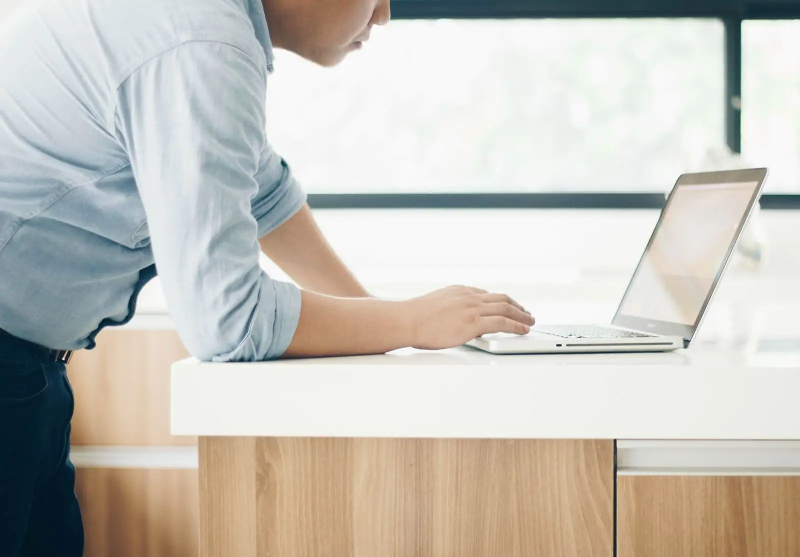 A laptop open on a bright office desk beside a notebook