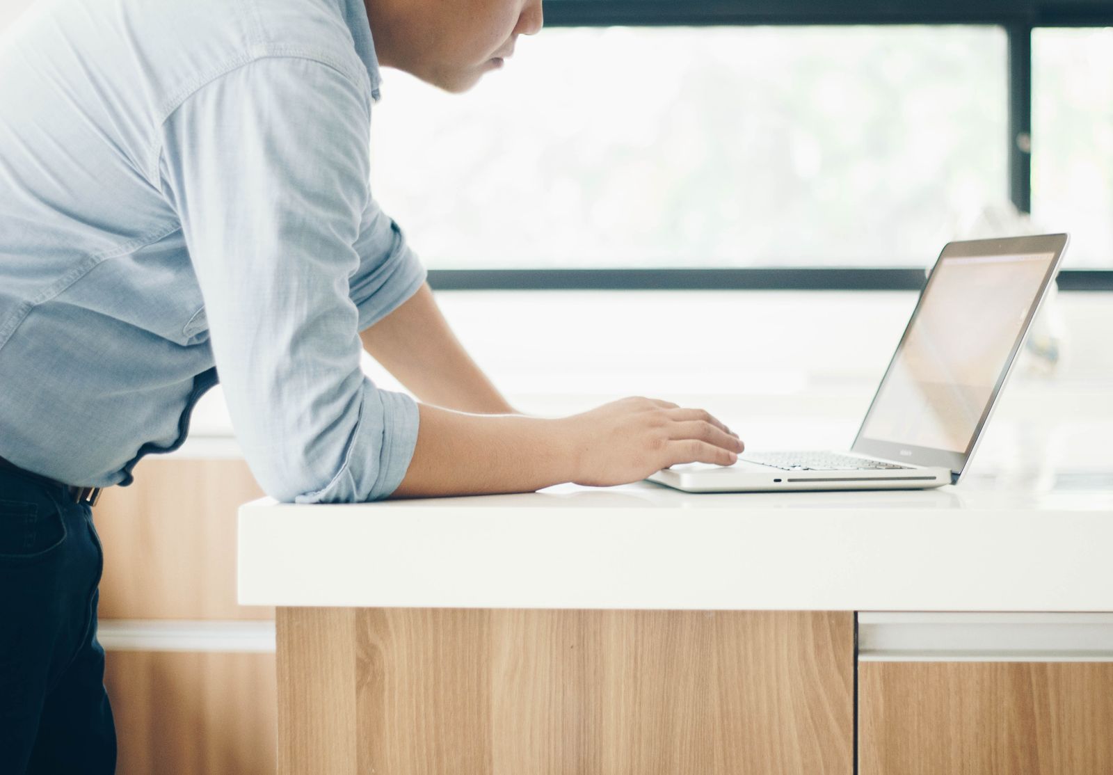 A laptop open on a bright office desk beside a notebook